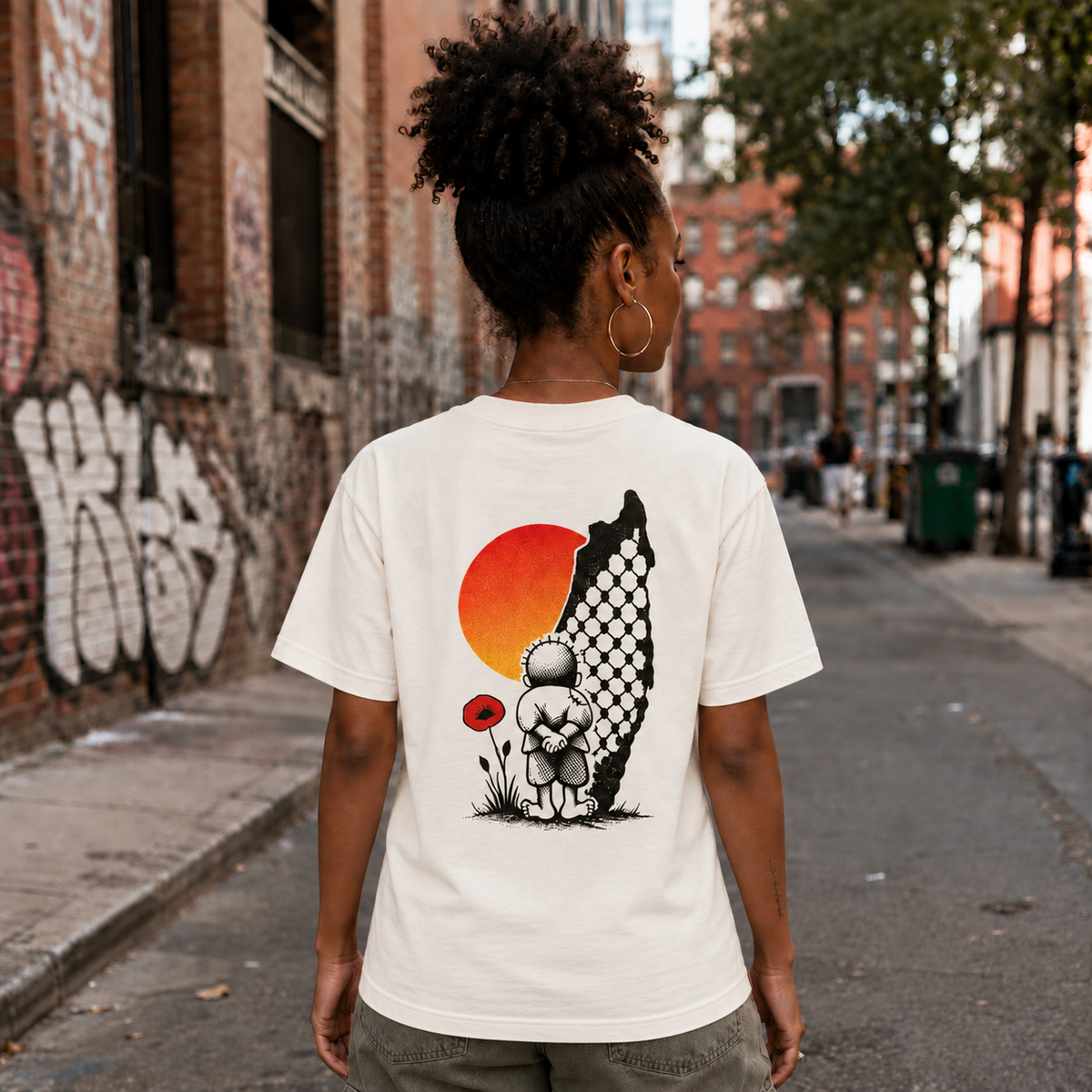 Lifestyle back view of natural Handala Palestinian T-shirt showing Handala artwork with a red poppy, orange sun, and keffiyeh-patterned map of Palestine.