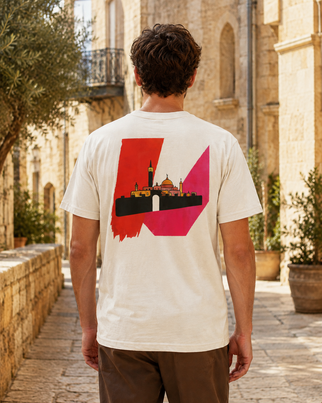 Man wearing a natural In Jerusalem Palestinian T-shirt, shown from the back with red, pink and black Jerusalem artwork.