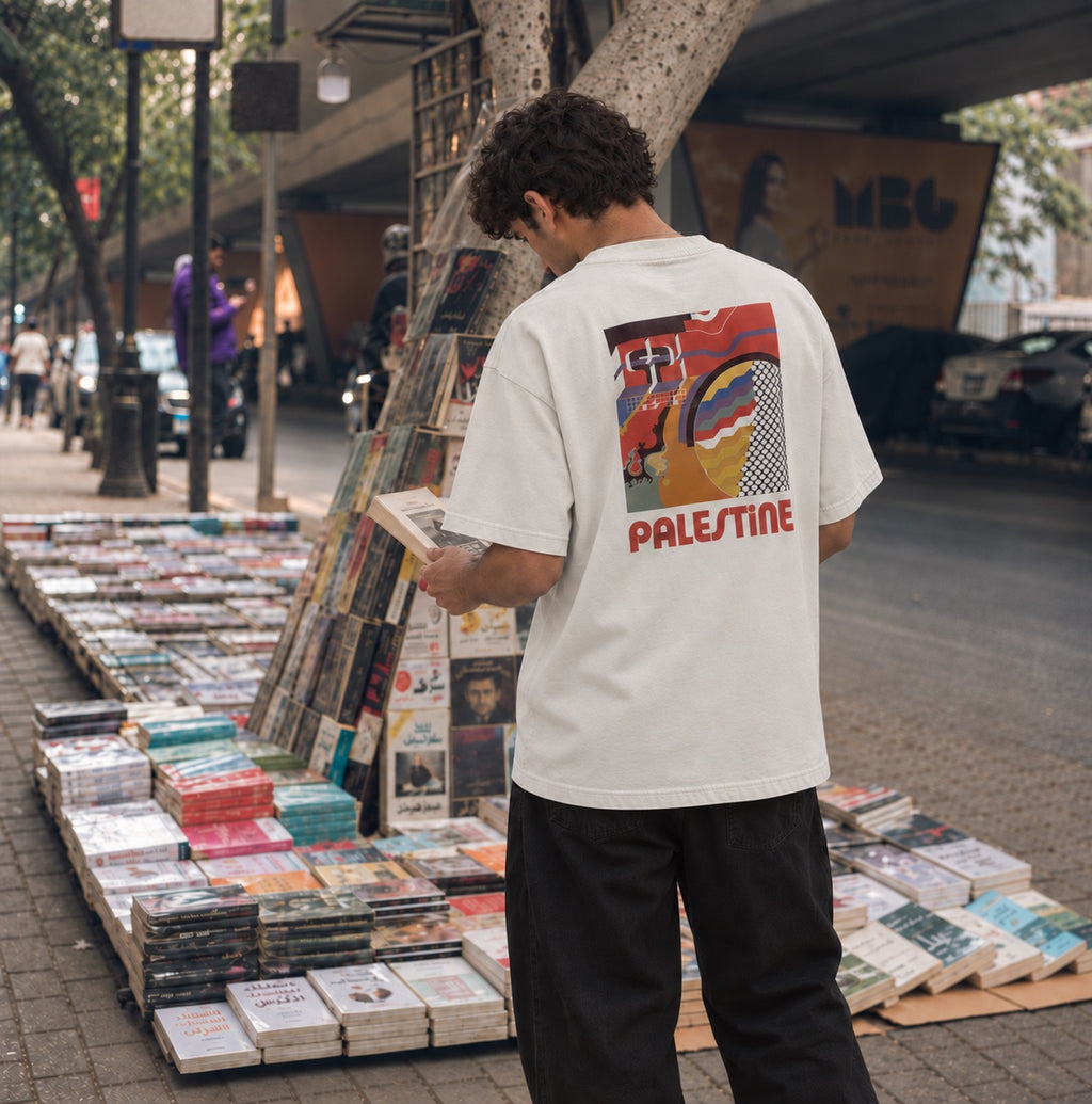 Back view of Faded Bone heavyweight Palestinian Geometry T-shirt with large Palestine artwork at a sidewalk bookstall.