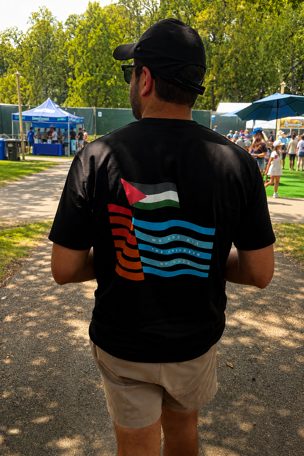 Man wearing the black heavyweight Children of Gaza Palestinian T-shirt, shown from the back while walking through an outdoor festival.
