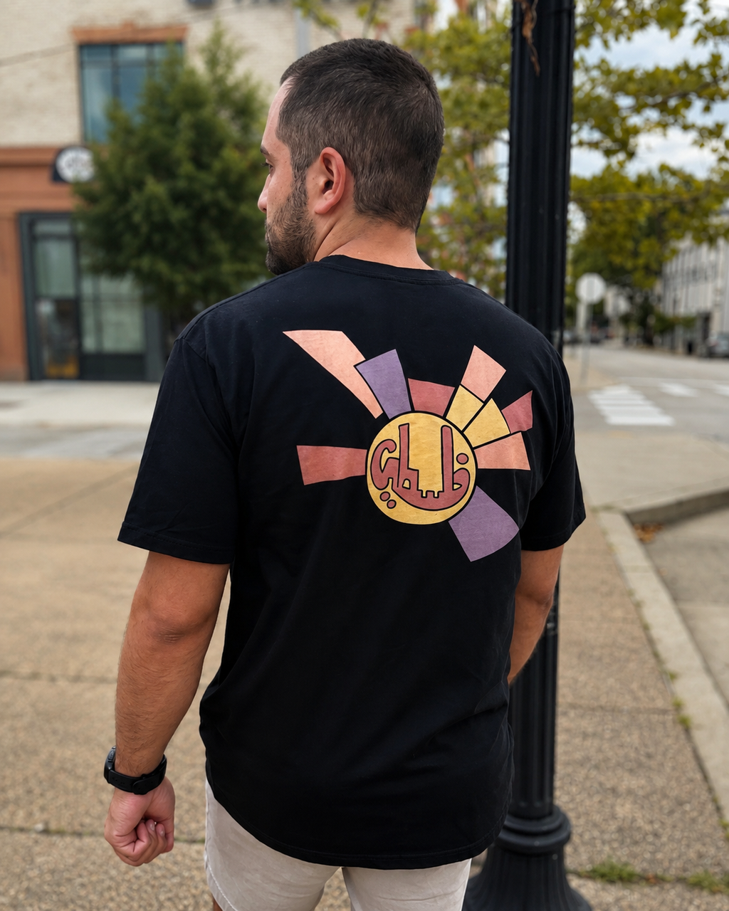 Man wearing the black lightweight Sun Medallion Palestinian T-shirt, shown from the back on a city street.